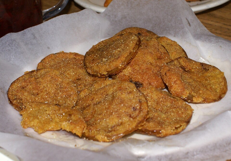 Golden cornmeal-crusted fried green tomato slices stacked on a plate