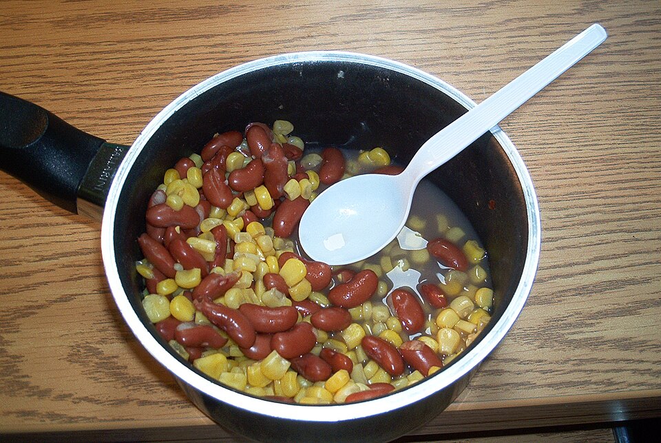 A pot of simmered shell beans and sweet corn with a serving spoon